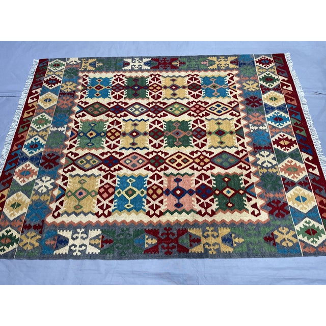 This Afghan Chobi wool kilim features a colorful geometric design with traditional tribal motifs in burgundy red, teal...
