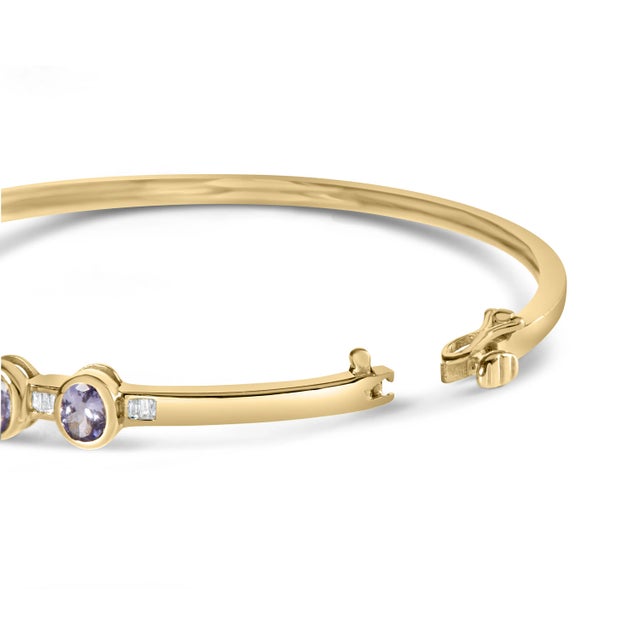 Indulge in the epitome of luxury with this exquisite 14K Yellow Gold Alternating Bezel Set Tanzanite and Diamond Bangle...