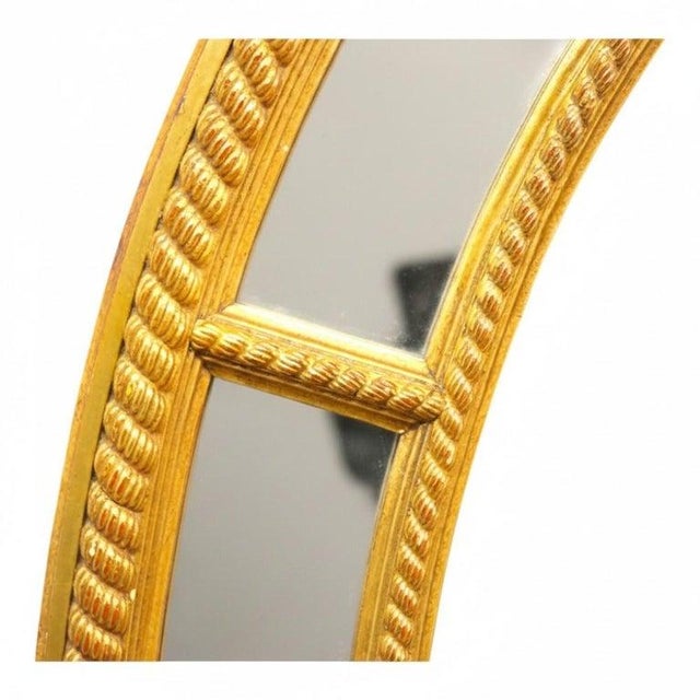 An elegant antique oval mirror, circa 1930, meticulously crafted from gilt wood. This mirror presents a distinctive...
