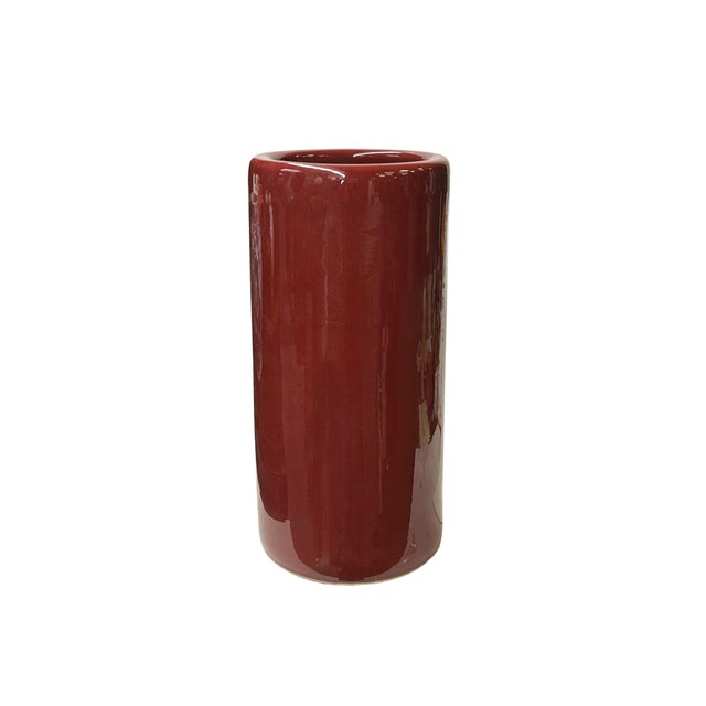 The is a cylindrical vase or pot with a smooth, glossy surface with a rich, deep red or maroon glaze that reflects light....