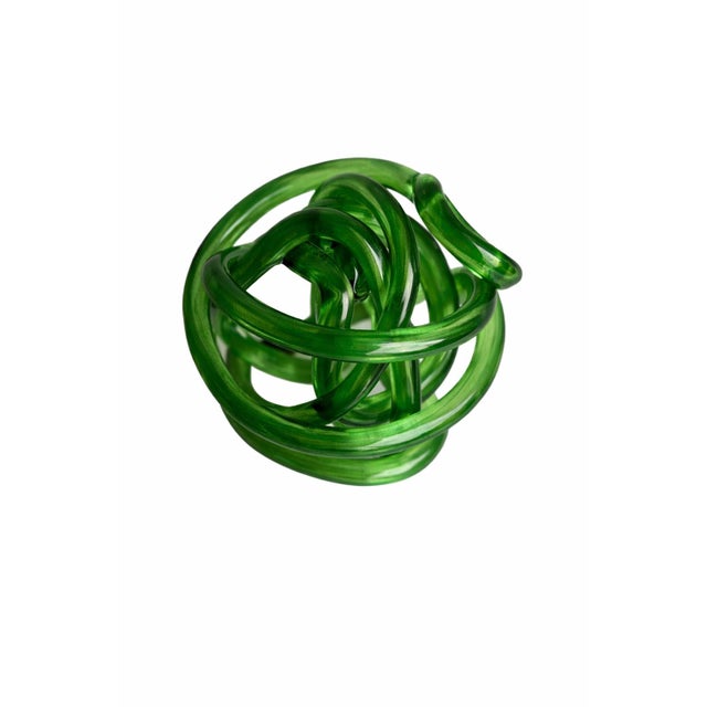 A striking green glass knot sculpture featuring an intricate, continuous loop design crafted from translucent emerald-...