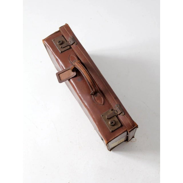 This is an antique leather suitcase circa early 20th century with travel stickers. The sleek leather luggage features a...