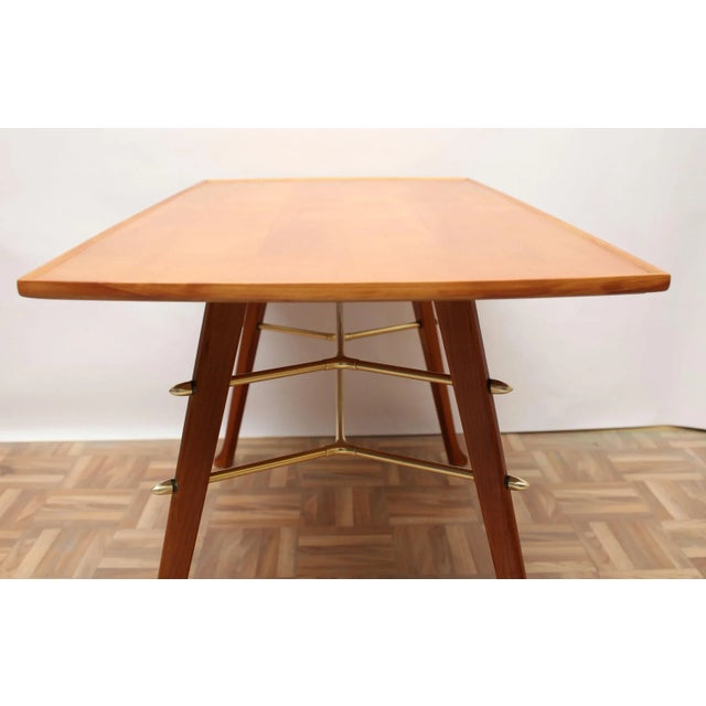 Elegant 50s coffee table. Surface in cherry veneer, construction of massive cherry wood with brass struts. With minor...