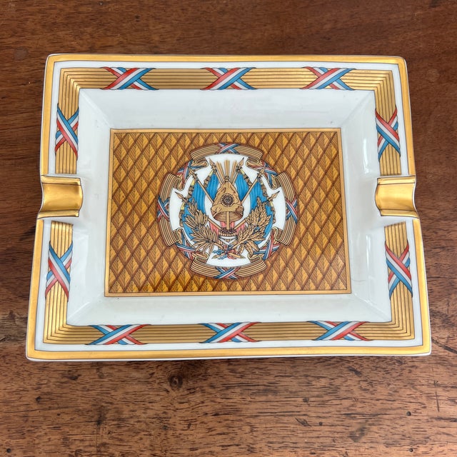 A rectangular porcelain catchall or cigar ashtray by Hermès Paris featuring a central French emblem design with gold trim