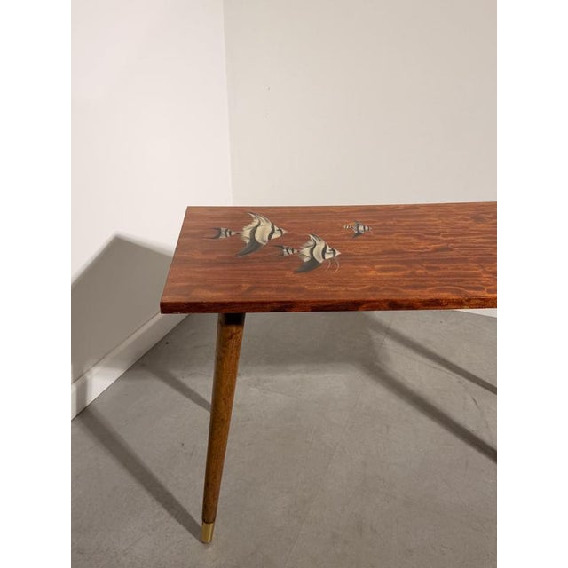 Charming vintage coffee table featuring elegant mid-century modern lines and decorative fish inlays on the tabletop....