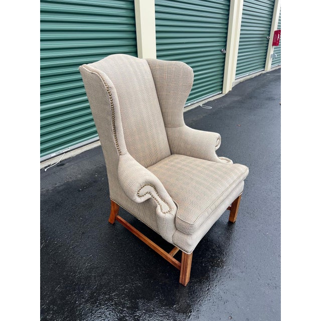 Classic wingback armchair crafted circa 1990s in the Traditional English style, featuring elegant rolled arms, nailhead...