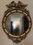 A Federal-style giltwood convex mirror crowned with a carved eagle, its wings outstretched above a laurel motif—an...