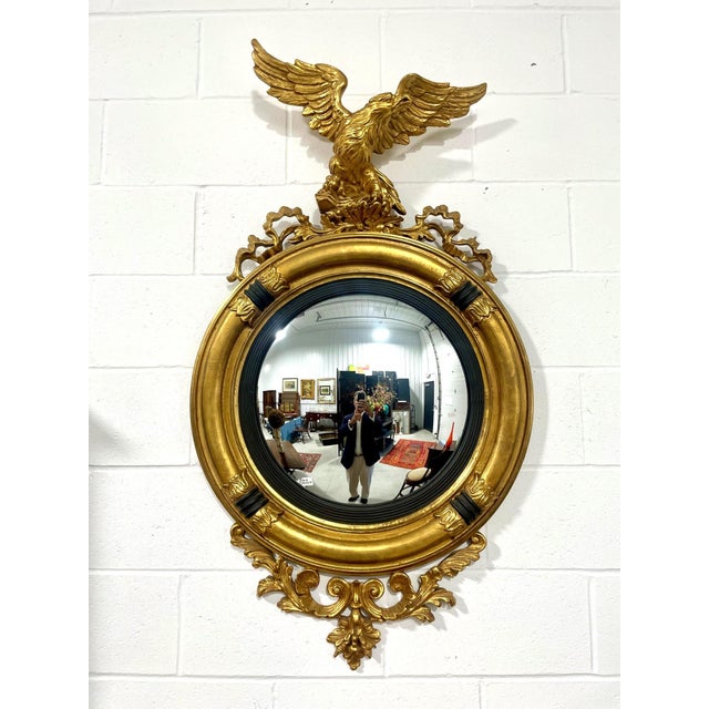 A classic Federalist style mirror with an impressive sculptural form of a gilded eagle excited into flight that crowns the...