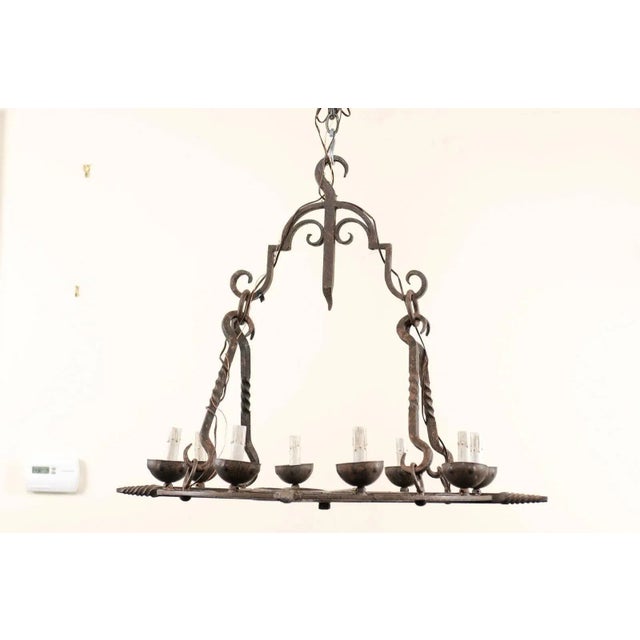 A French midcentury eight-light chandelier. This French chandelier from the mid-20th century of forged iron has a...
