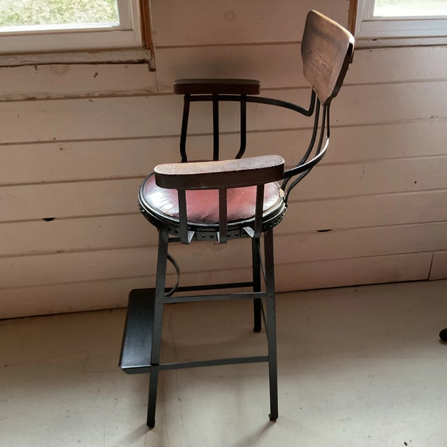 This industrial chair is crafted from heavy gauge steel and solid wood. It has a patina of age-subtle scuffs and worn...