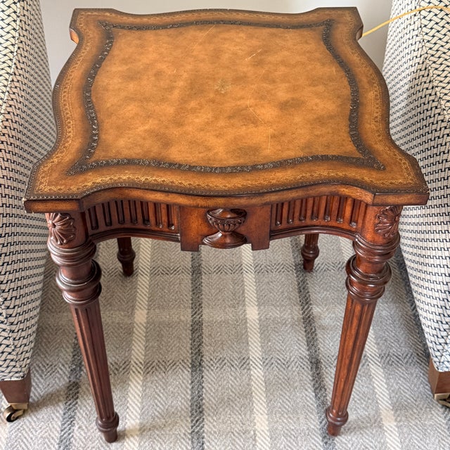 Maitland Smith Leather Top Table A scalloped shaped table with leather top. The apron is adorned with dense vertical...
