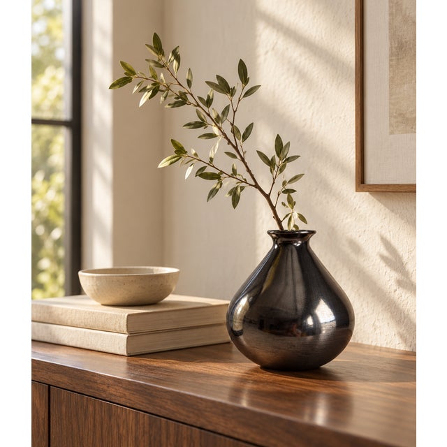 A sculptural black vase with a rounded teardrop body, tapered shoulders, and a gently flared rim. Its smooth, highly...