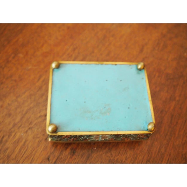 Brown cloisonné box raised on round feet with a hinged lid decorated in swirling and floral patterns in muted green, blue,...