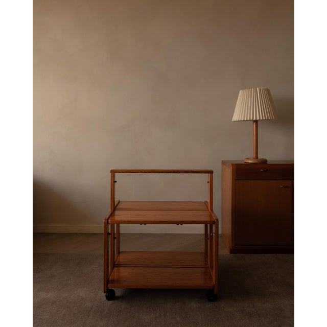 The warm wood with visible grain stands on four wheels and has two shelves that fold into the center frame. This allows...