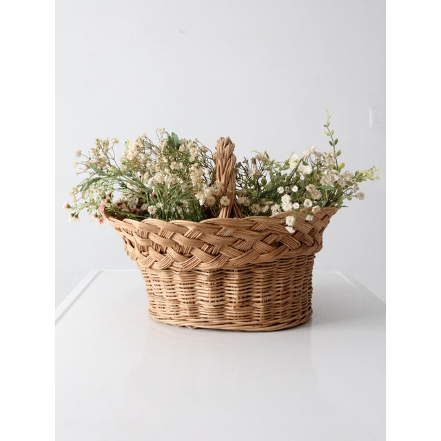 A vintage wicker gathering basket with a softly flared silhouette and a rounded handle, offering both function and...