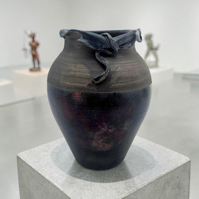 A sculptural studio pottery vessel defined by its architectural rim and restrained material palette. Hand-thrown in...