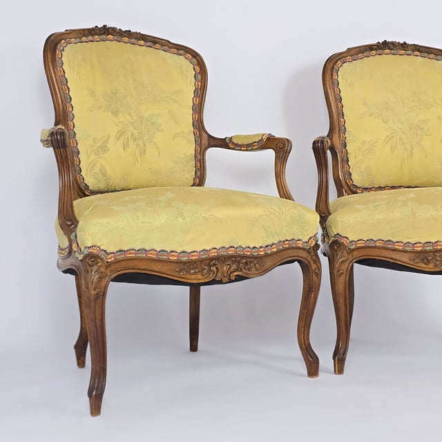 Pair of Louis XV Style chairs, each featuring an elegant, flowing walnut frame adorned with delicate floral carving,...