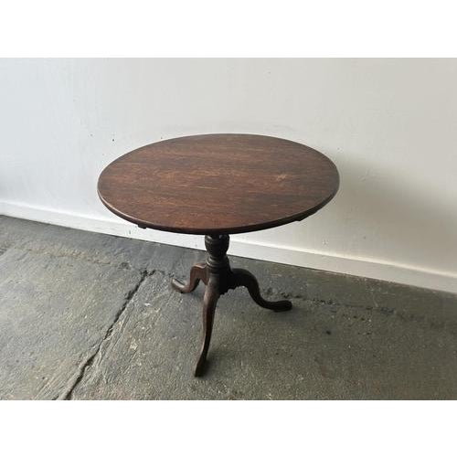 A compact circular wooden tilt-top occasional table with a single central turned pedestal and three cabriole-style legs...