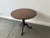 A compact circular wooden tilt-top occasional table with a single central turned pedestal and three cabriole-style legs...