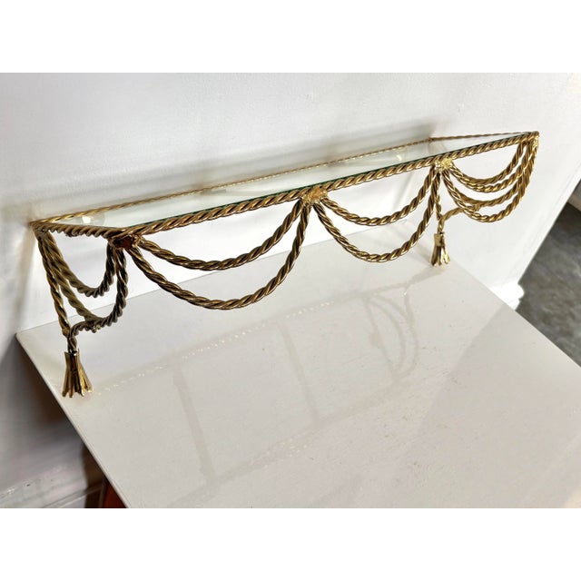 Metal wall shelf featuring gilded swagged rope and two tassels. Glass shelf. Great in a powder room. Most items found at...