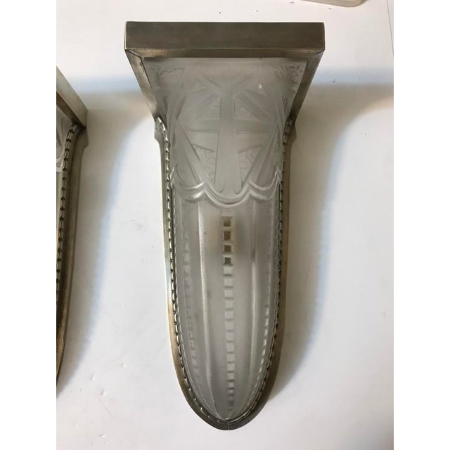 Stunning pair of French Art Deco wall sconces. With clear frosted glass shades with intricate geometric motif. Held by...