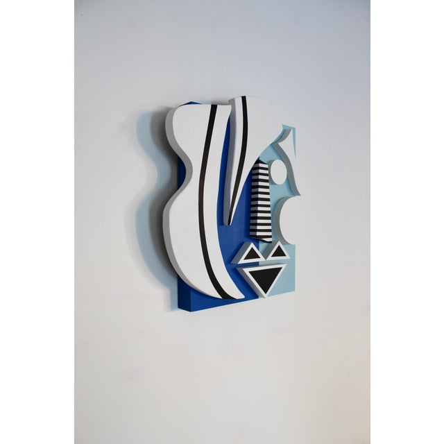 A wooden sculptural wall piece by Angela featuring a matte finish and a geometric take on portraiture. This piece includes...