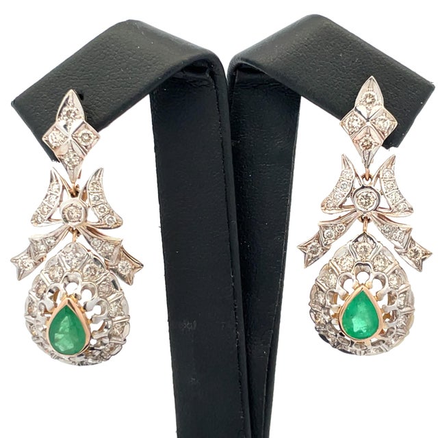 Luxurious 14K rose and white gold drop earrings featuring 2 emeralds totaling 1.50 carats, accented by 56 natural diamonds...