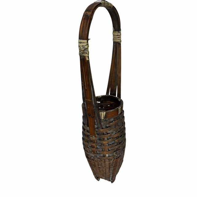 This is a tall, vintage Asian woven wicker basket featuring a handle and small feet, commonly used for floral displays or...