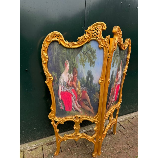 A refined 1960 Louis XVI-style two-panel room divider, handmade from carved solid beechwood with a rich antique gold...