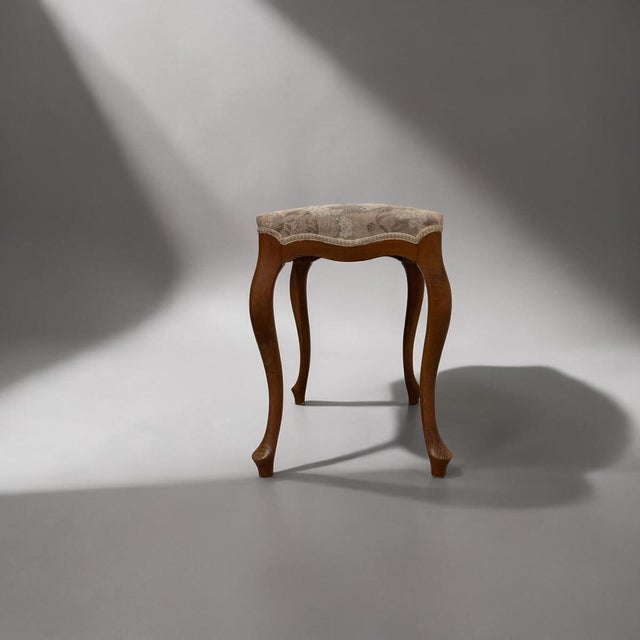 Upholstered stool produced in europe during the mid-20th century. executed in wood with curved cabriole legs and...