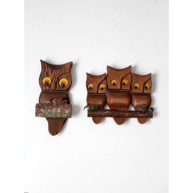 A pair of carved wood owl wall hangings in a classic mid-century folk style, defined by bold carved grain, inset eyes, and...