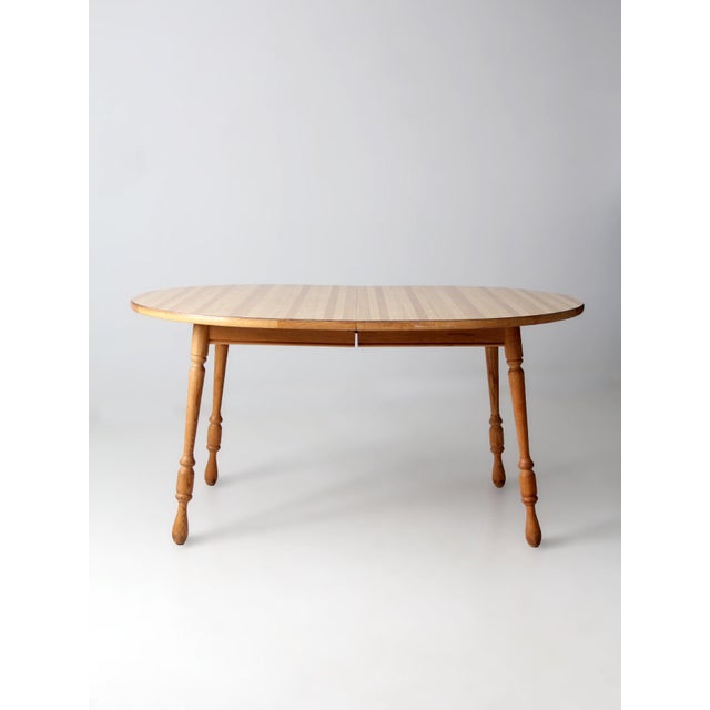 This vintage farmhouse dining table features a striped laminated wood top paired with turned legs in a warm natural...