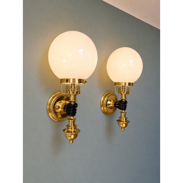 Pair of brass wall sconces in the hollywood regency style, depicting a hand holding a torch topped with a white opaline...