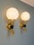 Pair of brass wall sconces in the hollywood regency style, depicting a hand holding a torch topped with a white opaline...