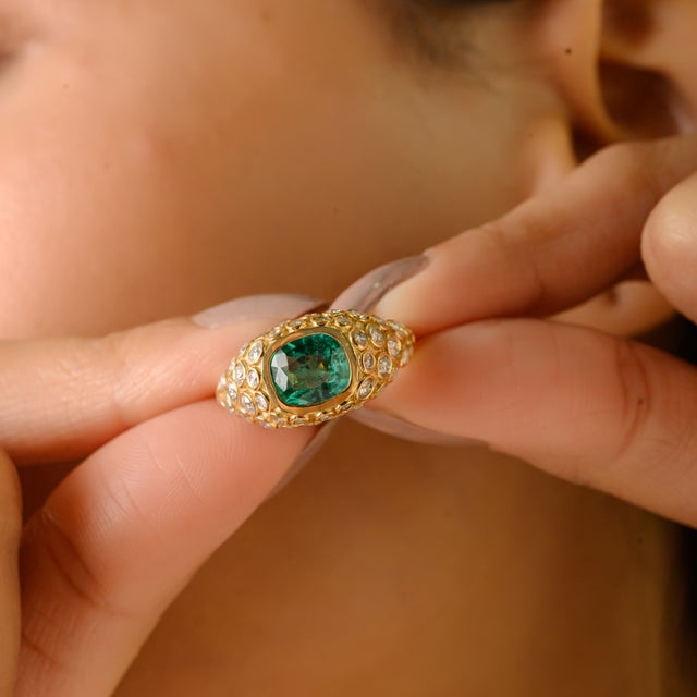 This exquisite ring is crafted in 18K yellow gold, featuring a 1.19-carat cushion-cut emerald as the centerpiece, bezel-...