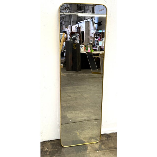 This tall floor mirror features a slim brass frame with softly rounded corners, defined by clean lines and a refined,...