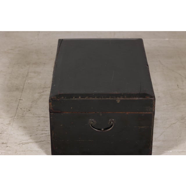 A late Qing Dynasty hand-painted black lacquer trunk with gold-gilded decoration, this early 20th-century storage chest is...