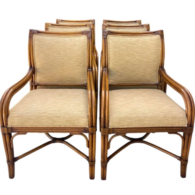 Set of six rattan dining armchairs featuring a warm honey-toned finish and tailored neutral upholstery. The sculptural...