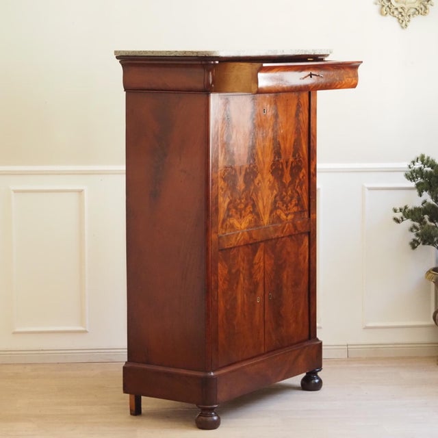 This elegant mahogany secretary desk, featuring a refined interior layout, dates stylistically to the early 19th...