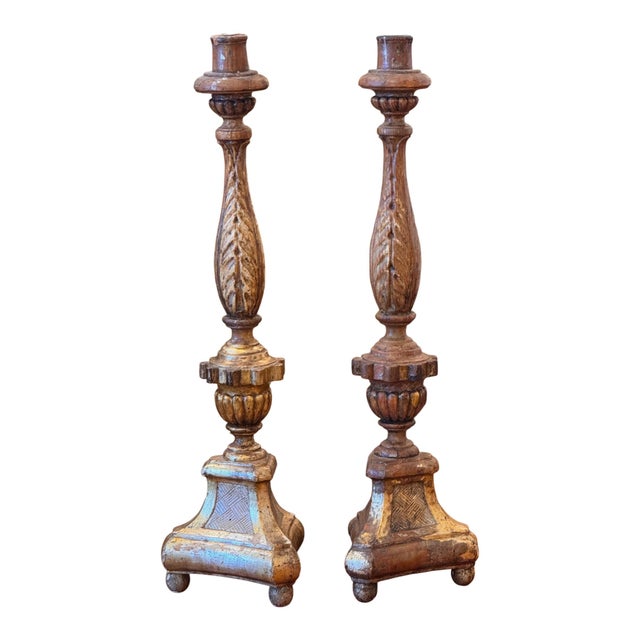 A pair of silver gilt candlesticks with a tapering leaf-carved shaft above a lobed knop and collar, set on triangular...