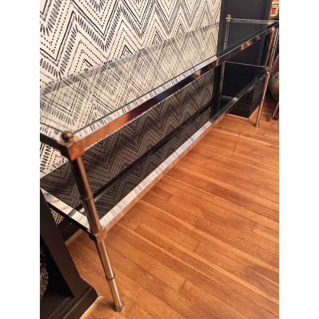 Elegant vintage chrome and glass console table featuring a sleek architectural frame with decorative brass-tone finials....