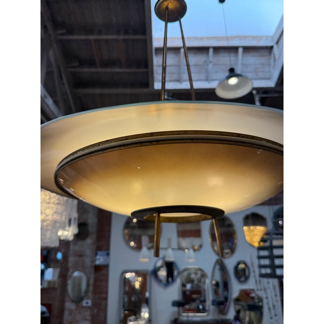 A refined 1950s Italian chandelier featuring a floating saucer-like silhouette crafted in brass and layered glass. The...