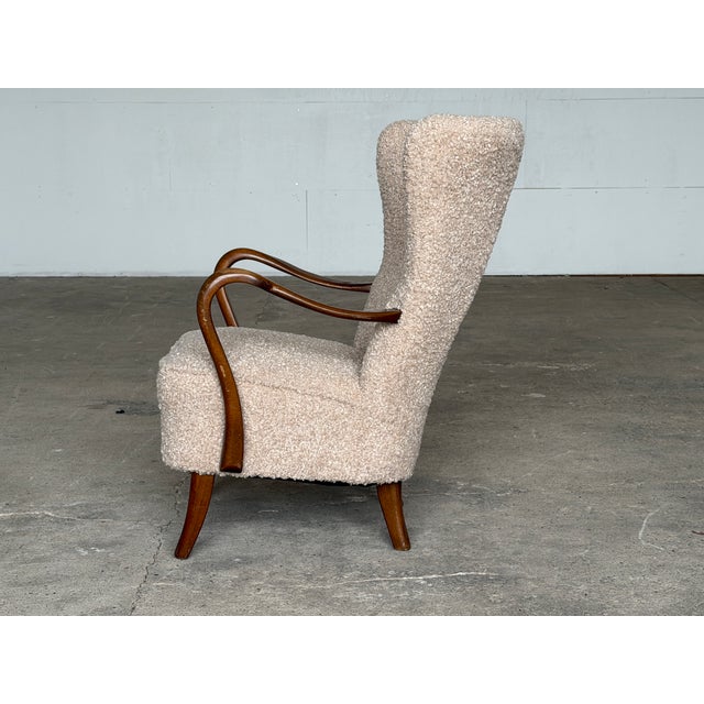 A beech wingback armchair in the Danish Modern tradition, upholstered in a warm, textured bouclé and produced by Alfred...