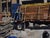 This oil painting depicts a solitary figure on a truck, engaged in the task of securing wooden planks with a sense of...