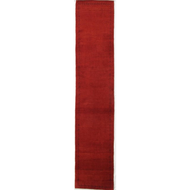 Vintage hand-knotted Persian Lori wool runner with a red field and a narrow linear border defined by simple twig-like...