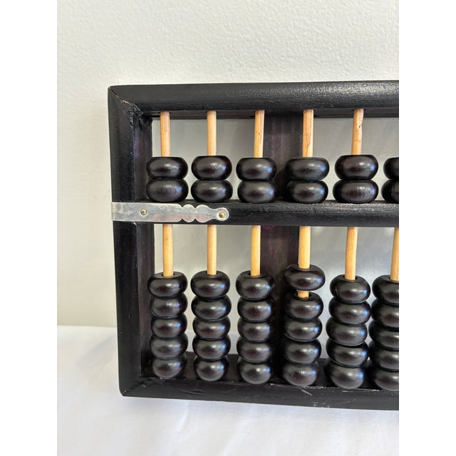 A traditional Chinese suanpan abacus constructed with 13 bamboo-colored rods, black wooden beads, a black frame, and...