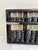 A traditional Chinese suanpan abacus constructed with 13 bamboo-colored rods, black wooden beads, a black frame, and...