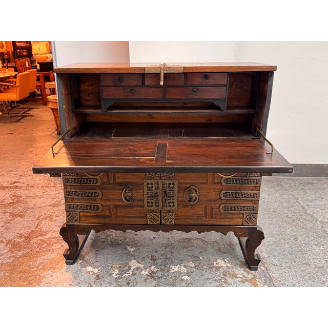 Design Plus Gallery presents an Antique Korean Drop Front Storage Desk. The case presents paneled woodwork, carved bracket...