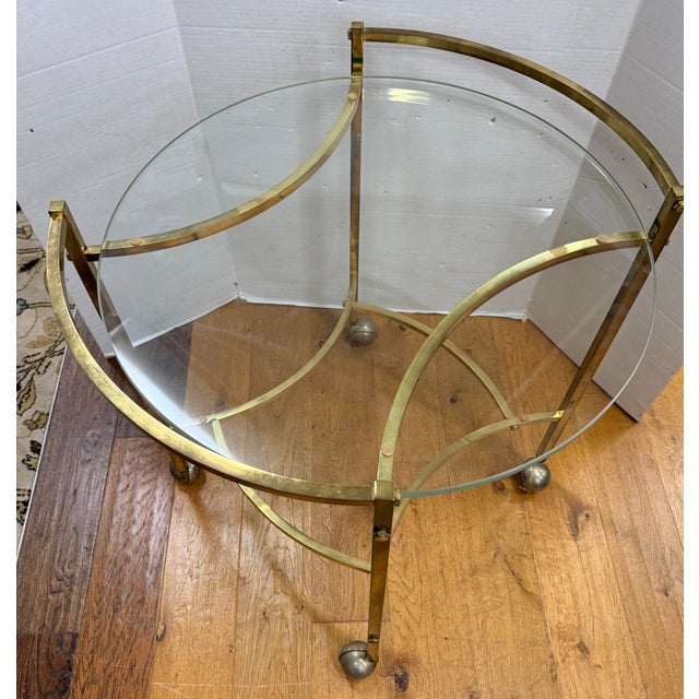 A sleek mid-century bar cart featuring a clean-lined brass frame with an elegant oval silhouette and inset glass top. The...