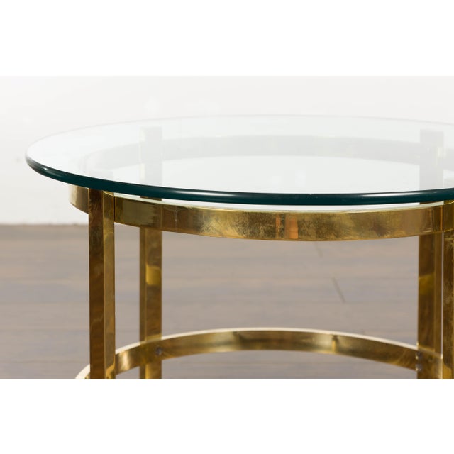 An Italian Midcentury brass side table from circa 1950 with circular glass top. Indulge in the elegance of the 1950s with...